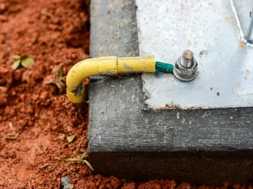 Connexion de la prise de terre maison à une structure métallique, assurant la sécurité électrique. Le câble jaune est relié à une cosse verte, fixée par un boulon.
