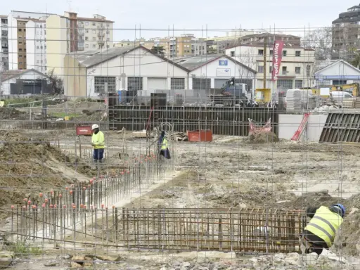Obreros trabajan en la preparación de cimientos para nuevos proyectos de construcción. Se ven varillas de acero y maquinaria pesada en un día nublado.