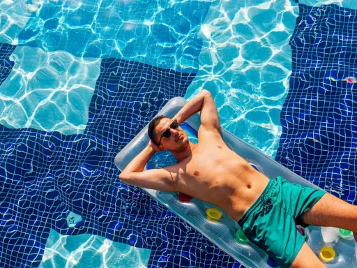 Uomo rilassato su un materassino in piscina, con gli occhiali da sole. Chissà se posso andare al mare se prendo l'antibiotico, pensa.