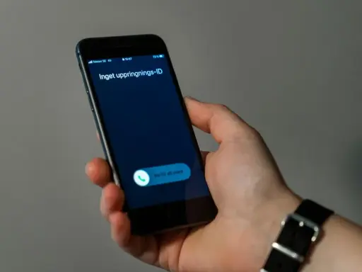 En hand håller en mobiltelefon med ett inkommande samtal. Skärmen visar "Inget uppringnings-ID" och en knapp för att svara.
