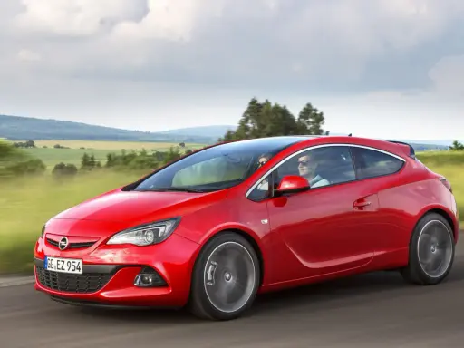 Czerwony Opel Astra J 1.4 Turbo z parą na pokładzie przemierza malowniczą trasę wśród zielonych pól i wzgórz.
