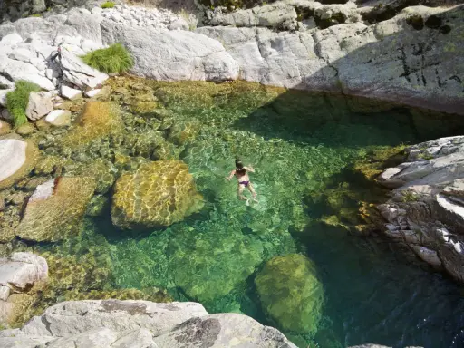 Una persona nada en unas cristalinas piscinas naturales Gredos, rodeadas de rocas y vegetación.