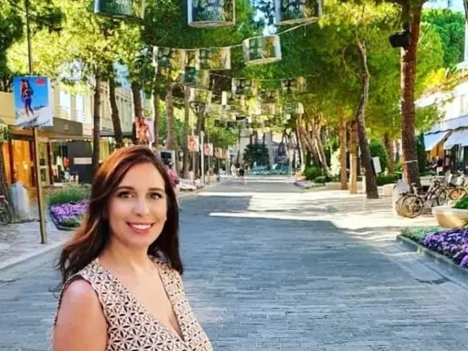 Donna sorridente in una strada alberata con negozi e fiori viola, un'atmosfera estiva nel centro di Milano Marittima.
