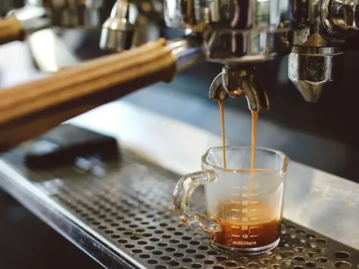 Espresso spływa do szklaneczki. Czy ekspres do kawy pobiera dużo prądu? To zależy od modelu, ale ten wygląda na profesjonalny.