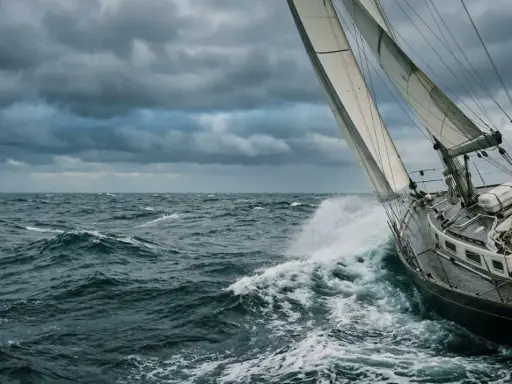 Un voilier fend les vagues sous un ciel menaçant. La proue découpe l'écume, le vent gonfle les voiles.