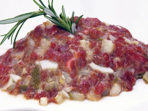 Delicioso steak tartar de los Hermanos Torres, con carne picada, cebolla, pepinillos y un toque de romero.