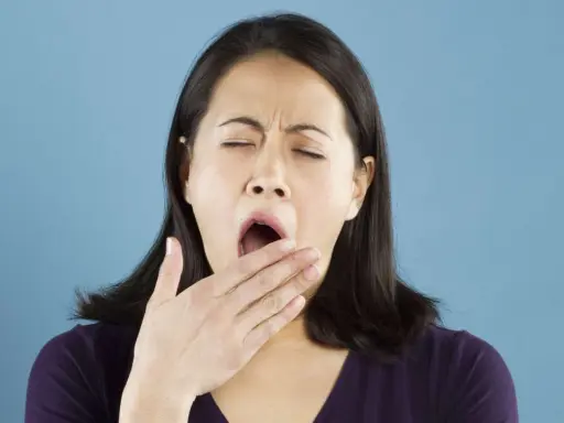 Une femme bâille, la main devant la bouche. Elle semble avoir besoin d'une pause pour réviser la conjugaison.