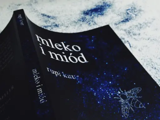 Okładka książki "Mleko i miód" Rupi Kaur z motywem pszczoły na granatowym tle w gwiazdy.