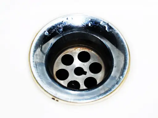Gouttes d'eau stagnent dans un évier bouché mais pas de bouchon visible. Le métal du siphon est sale et usé.
