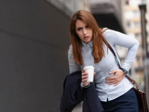 Kobieta z kubkiem kawy w dłoni odczuwa silne skurcze po alkoholu, trzymając się za brzuch.