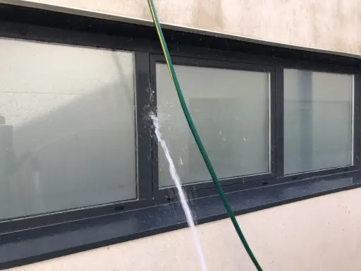Agua salpicando sobre un perfil de aluminio de ventana, creando condensación y gotas.