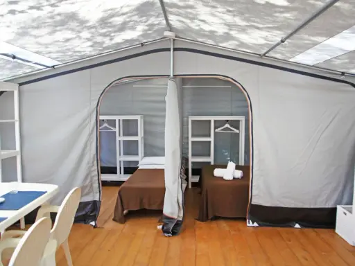 Interno di un alloggio al Family Club Marina di Ugento: due letti singoli con coperte marroni, mensole bianche e un tavolo con sedie.