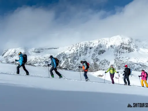 Grupa ludzi na skitouringu wspina się po ośnieżonych zboczach gór. To właśnie skitouring co to za aktywność!