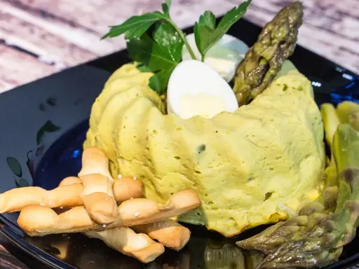 Delizioso flan di asparagi, guarnito con uovo sodo, asparagi freschi e grissini croccanti su un piatto nero.