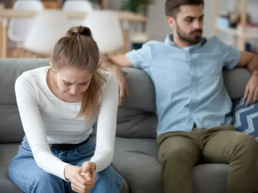 Smutna kobieta siedzi na kanapie, odwrócony mężczyzna obok.