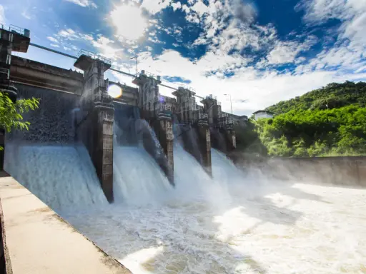 Ein Damm mit mehreren offenen Schleusen, aus denen kräftig Wasser strömt. Ein Beispiel für erneuerbare Energien durch Wasserkraft.
