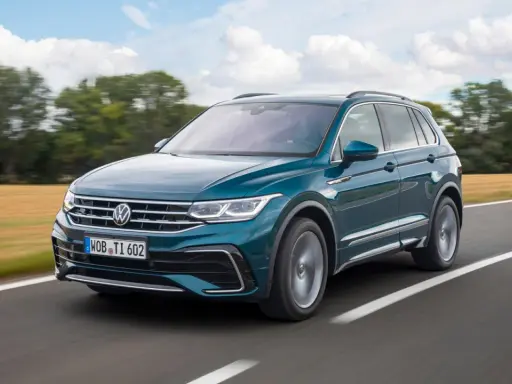 Un Volkswagen Tiguan R-Line verde oscuro se desplaza por una carretera rural, con campos dorados y árboles borrosos al fondo.