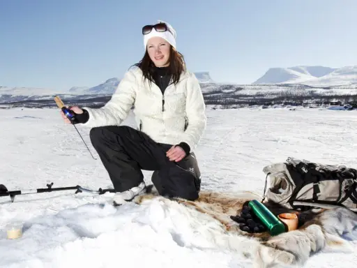 Kvinna ispirar isfiske i Kiruna. Hon har fiskeutrustning och en ryggsäck bredvid sig.