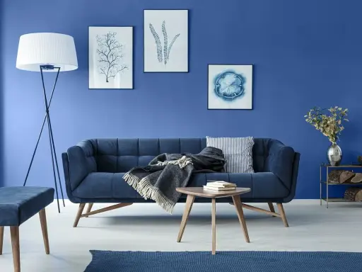 Sofa i ściany w odcieniach koloru niebieskiego. Na ścianie obrazy z motywami morskimi.