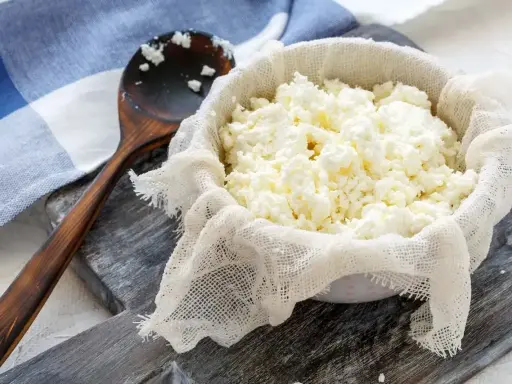 Świeży twaróg z mleka krowiego, odsączany na gazie. Drewniana łyżka obok. Idealny do domowych serów.