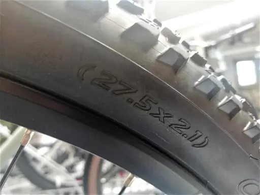 Na oponie rowerowej widoczny napis (27.5x2.1), który pomaga określić, jak zmierzyć rozmiar koła w rowerze.