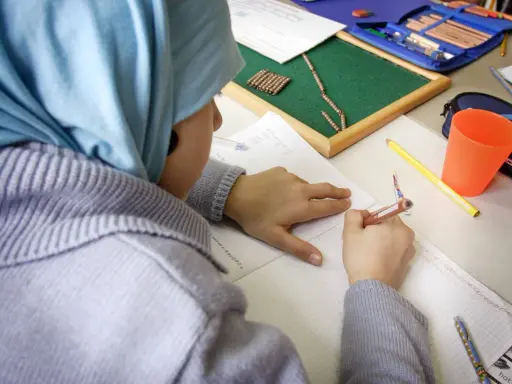 Kind mit Kopftuch schreibt im Heft. Trotz Opferfest und Schulfrei wird gelernt.