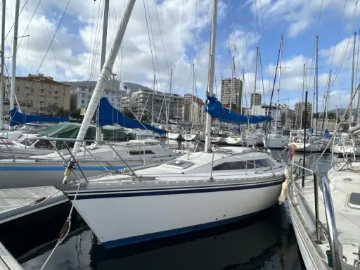 Un voilier blanc aux voiles bleues, amarré dans un port. L'avis sur ce voilier rush est qu'il est prêt pour la prochaine aventure.