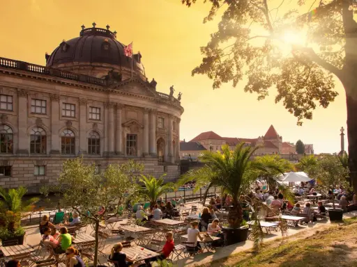 En solig eftermiddag vid en uteservering i Berlin, med en imponerande byggnad i bakgrunden. Kanske en paus innan nattåg Berlin.