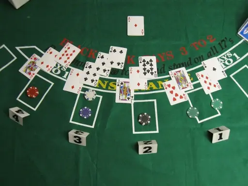 Stół do gry w blackjacka, karty i żetony. Widać karty z numerami i figurami, a także napisy "BLACKJACKS 3 TO 2" i "stand on all 17's".