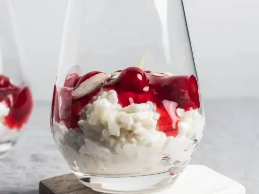 Delicioso arroz con leche asturiano cremoso, coronado con cerezas rojas y almendras laminadas en un vaso.