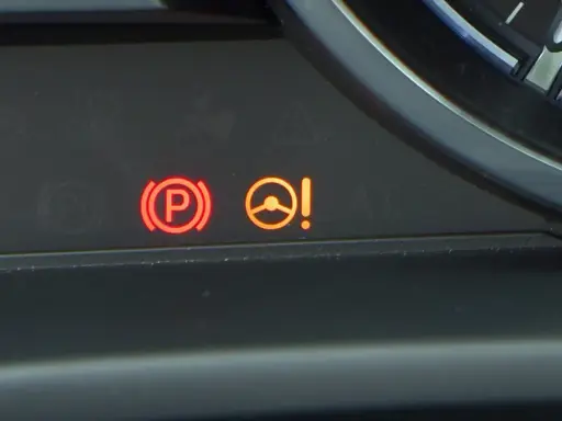 Kontrolka PS Nissan: czerwony symbol hamulca ręcznego i pomarańczowa kontrolka układu kierowniczego z wykrzyknikiem.