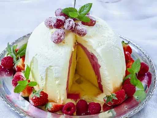 En imponerande dessert till nyår: en kupolformad glassbakelse med lager av gul och rosa glass, dekorerad med färska bär och mynta.