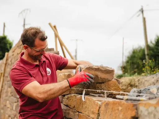 Un maçon, ganté de rouge, pose une pierre pour construire un mur en Corse.