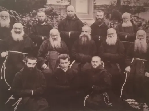 Grupa zakonników w habitach. W środku, w pierwszym rzędzie, siedzi młody mężczyzna, być może to **Honorat Koźmiński** w otoczeniu braci.