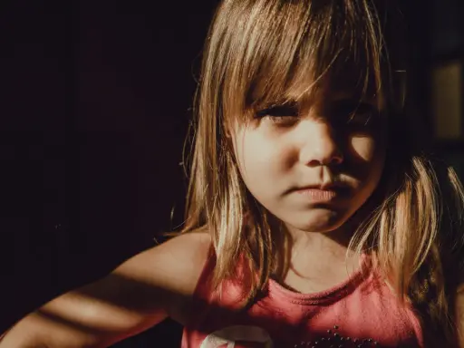 Niña con expresión seria, con luz de ventana en su rostro. A veces, mi hijo de 9 años se enoja por todo, pero hoy solo mira con intensidad.