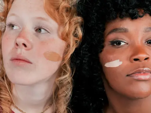 Dos mujeres, una pelirroja pecosa y otra de piel oscura, muestran diferentes tonos de piel con muestras de maquillaje.