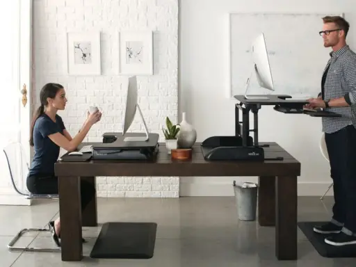 Un homme et une femme travaillent sur des bureaux réglables en hauteur. Une pause obligatoire pour le travail debout est essentielle pour leur bien-être.