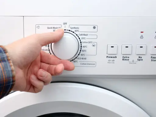 Dłoń ustawia pokrętło pralki. W ilu stopniach prac białe ubrania? Programy wskazują od 20°C do 90°C.