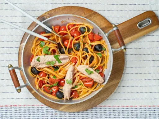 Pyszne spaghetti alla puttanesca z tuńczykiem, pomidorkami i czarnymi oliwkami w metalowej patelni, gotowe do podania.