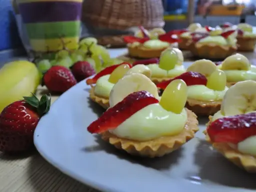 Pyszne babeczki z budyniem, udekorowane truskawkami, bananami i winogronami, wyglądają apetycznie.