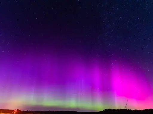 Nocne niebo rozświetlone fioletową i zieloną zorzą polarną, kiedy jest zorza polarna. Gwiazdy migoczą nad ciemnym horyzontem.