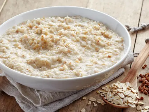 Schüssel mit Haferbrei, daneben Haferflocken und Buchweizen. Gute Haferkur Erfahrungen beginnen mit einem gesunden Frühstück.