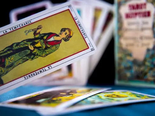 Rozłożone karty tarot 3 karty: "La Tempérance" w centrum, inne karty w tle i pudełko z napisem "Tarot".