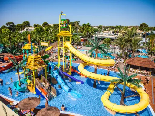 Un parque acuático con toboganes amarillos y azules, palmeras y gente disfrutando. ¡Un lugar ideal para camping con toboganes en España!