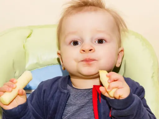 Mały chłopiec z radością zajada chrupki kukurydziane dla niemowląt, siedząc w krzesełku.