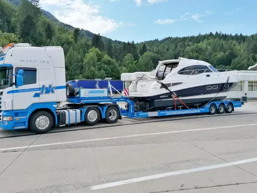 Ein LKW transportiert eine weiße Yacht auf einem Tieflader. Informieren Sie sich über bootstransport kosten für Ihre nächste Überführung.