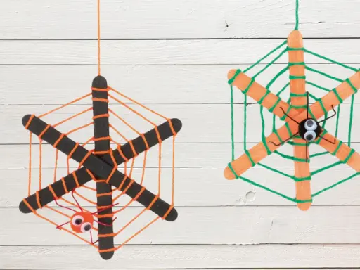 Zwei selbstgebastelte Spinnennetze aus Eisstielen und Wolle, mit kleinen Spinnen und Kulleraugen. Perfekt zum Spinnennetz basteln für Halloween!