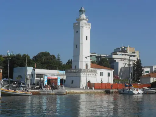 Il faro di Rimini, con la sua torre bianca e il porto con barche a vela, si staglia contro il cielo azzurro.