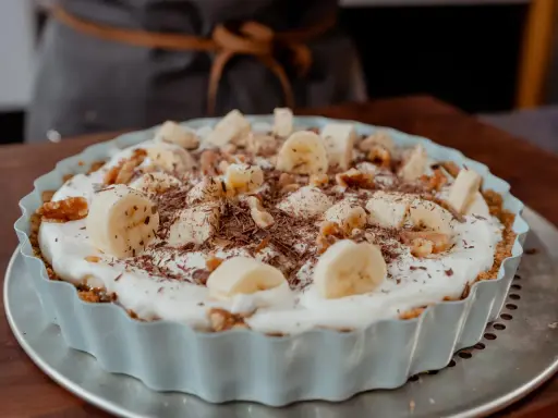 Tarte banane caramel onctueuse, garnie de rondelles de banane, noix et copeaux de chocolat. Un délice gourmand.