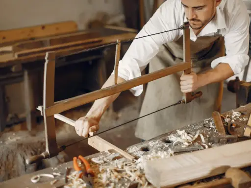 Artisan menuisier travaillant le bois avec une scie, dans un atelier d'ébénisterie d'art.